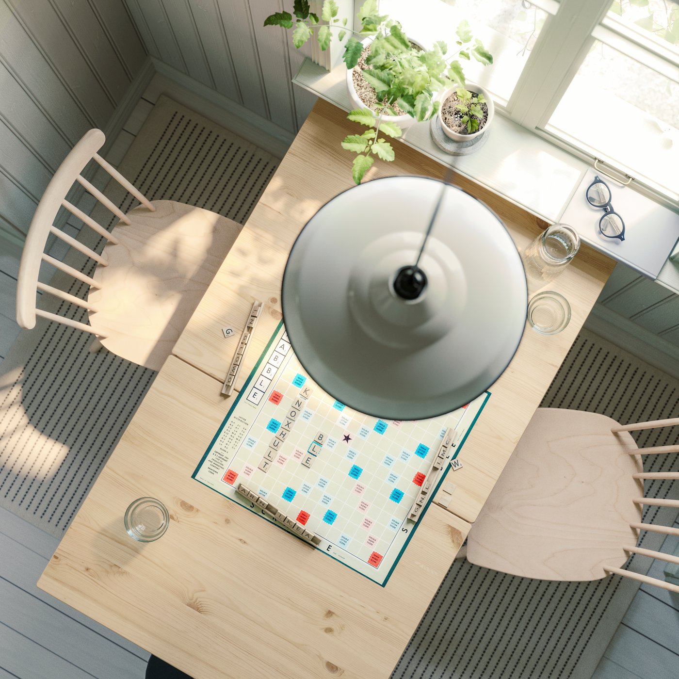 Vista a volo di uccello di un tavolo a ribalta PINNTORP, in finitura mordente marrone chiaro o bianco, posizionato sotto una finestra della cucina con due sedie HÖGVED.