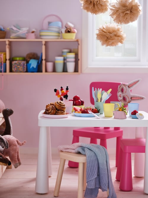 A pastel room with pink MAMMUT children’s chairs around a white MAMMUT children’s table set with colourful snacks.