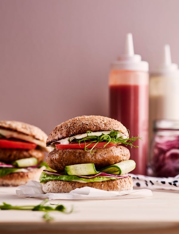 Auf einem Tisch liegen Pflanzliche Burger und im Hintergrund kann man Soßen sehen.