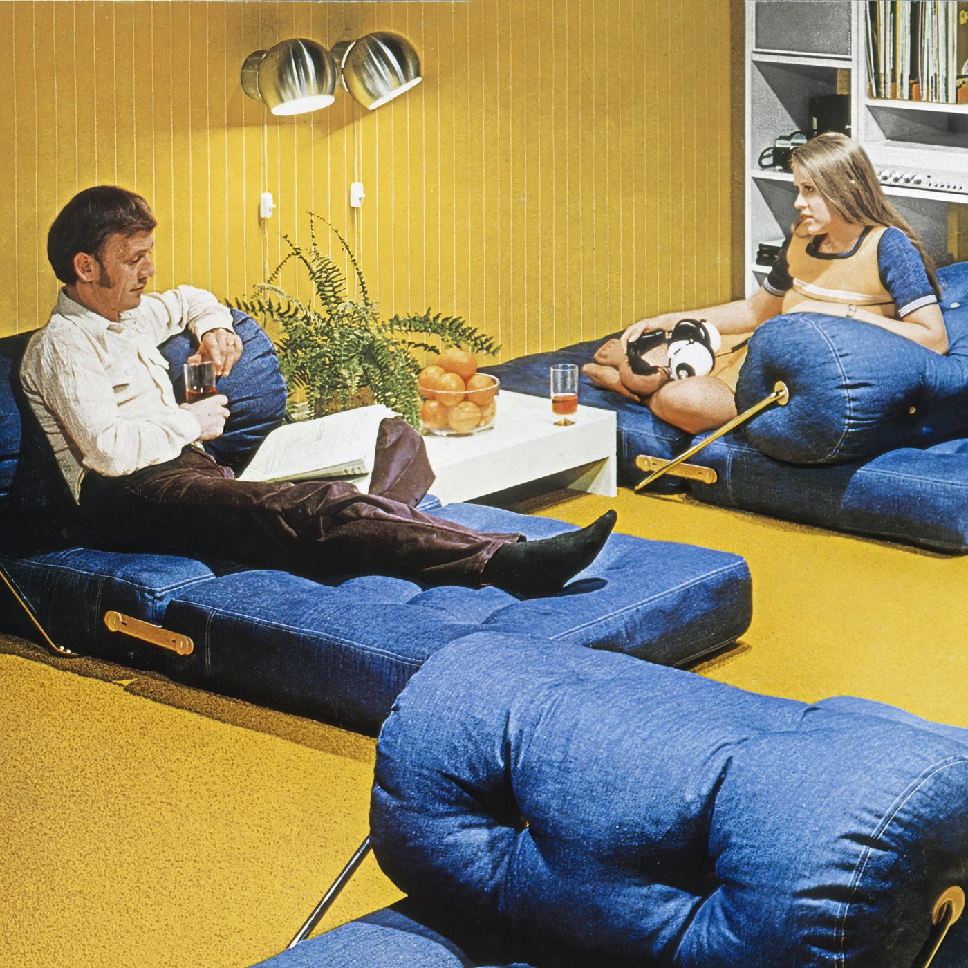 The cover photo of the 1973 IKEA Catalogue showing a couple reclining on two TAJT easy chairs in a room with yellow carpet.