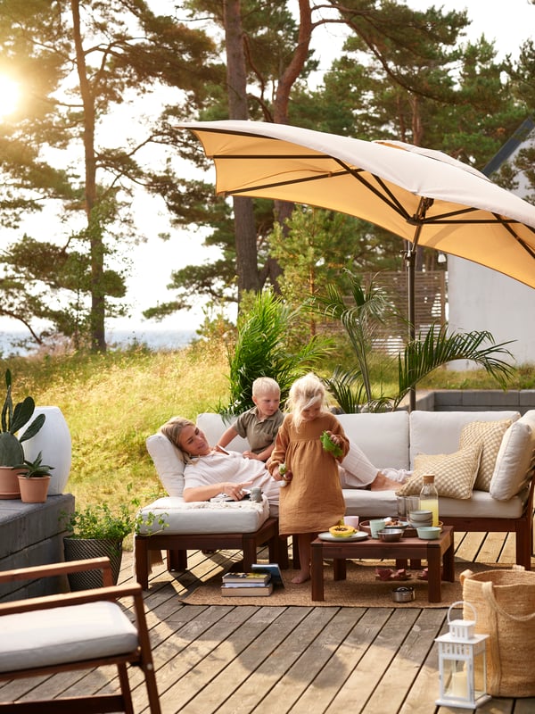 An outdoor deck with a family sitting on a lounge chair under a large beige standing umbrella.