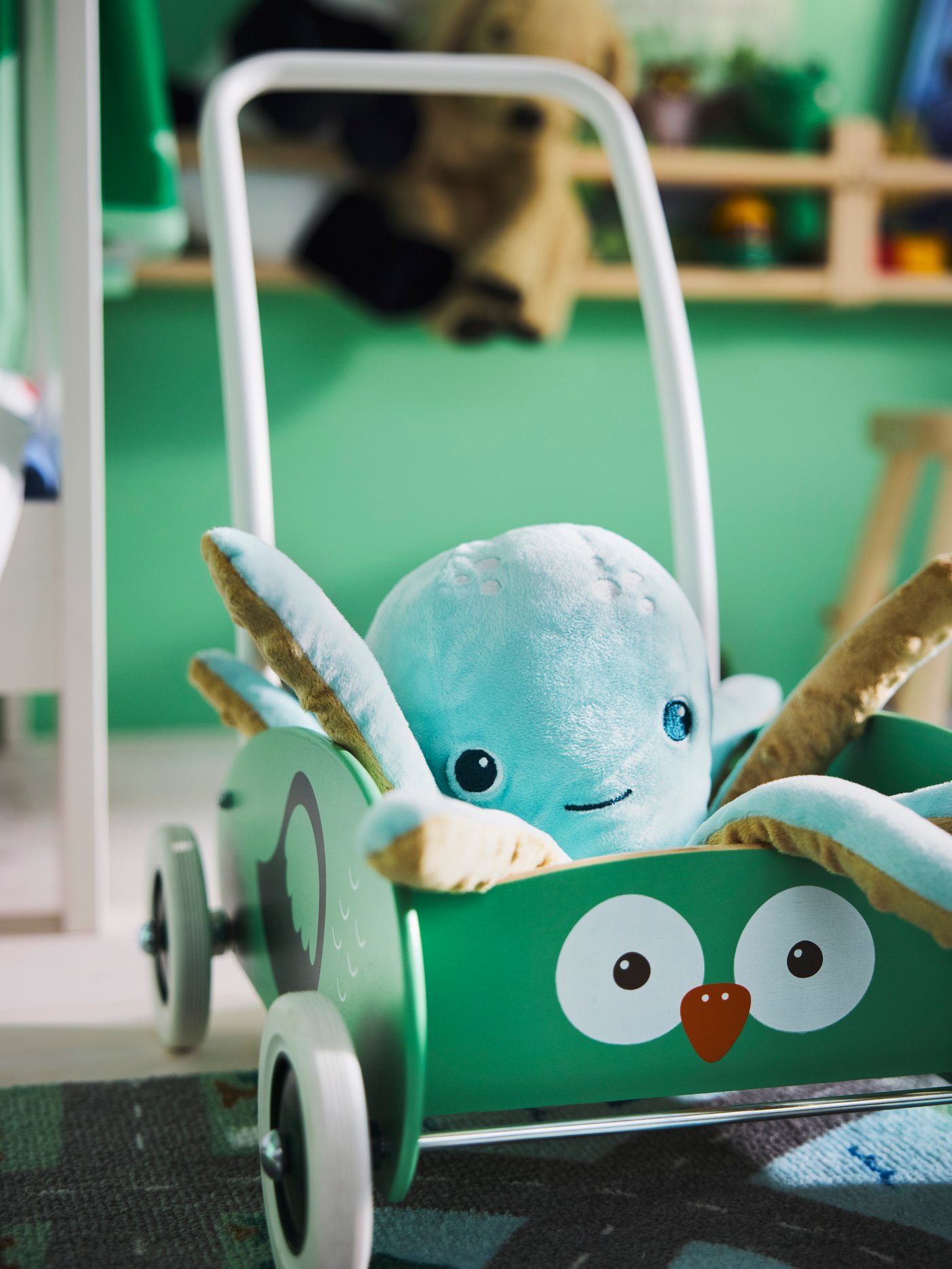 Close-up of UPPSTÅ toddler walker with a light turquoise soft toy octopus in it, and a bright green rug in background.