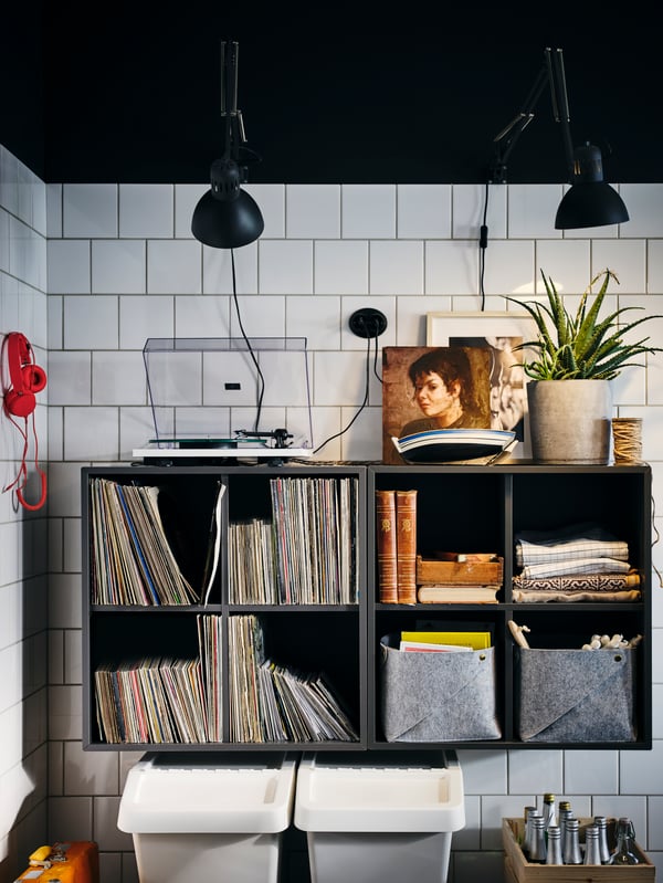 A corner of a white-tiled kitchen with side-by-side, wall-mounted, dark-grey EKET four-compartment cabinets.