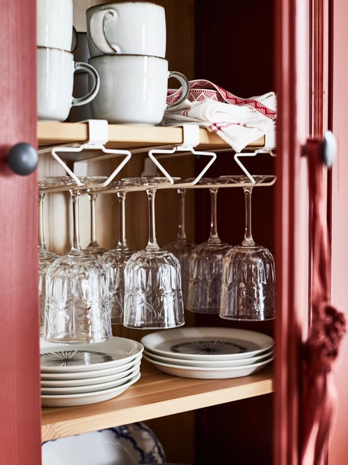 Gros plan sur une armoire de cuisine dans laquelle se trouvent des assiettes et un support à pince polyvalent en acier blanc sous la tablette, utilisé pour tenir des articles en verre.