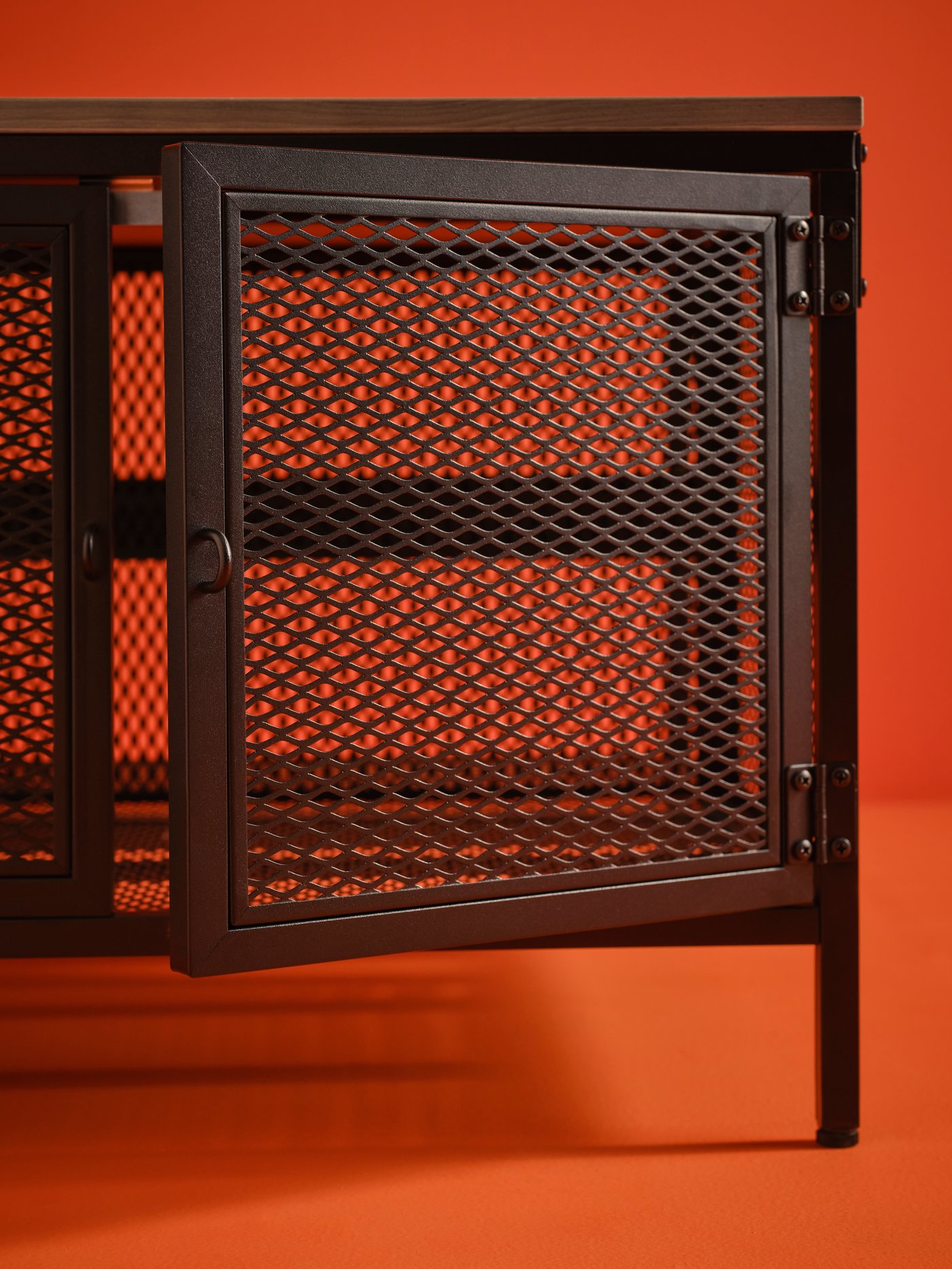 Espacio de trabajo con un fondo naranja y una mesa de almacenaje FJÄLLBO negra de pino macizo y acero.