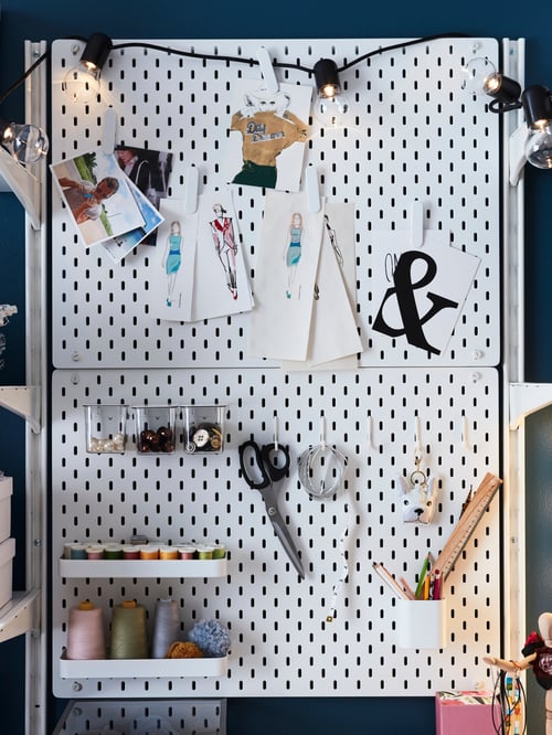 Two white SKÅDIS pegboard combinations are mounted on a wall. The accessories hold sewing supplies like scissors on a hook.