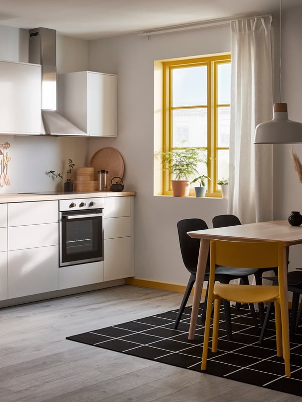 Man sieht eine minimalistische Küche mit matten, grifflosen Fronten und einer Arbeitsplatte aus Holz. Vor der Küche steht auch ein LISABO Esstisch mit vier Esszimmerstühlen.