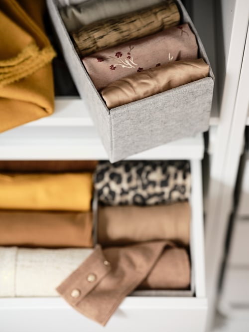 Un prim-plan al dormitorului cu o cutie gri dreptunghiulară, în interiorul unui mobilier alb, care conține mai multe eșarfe colorate.