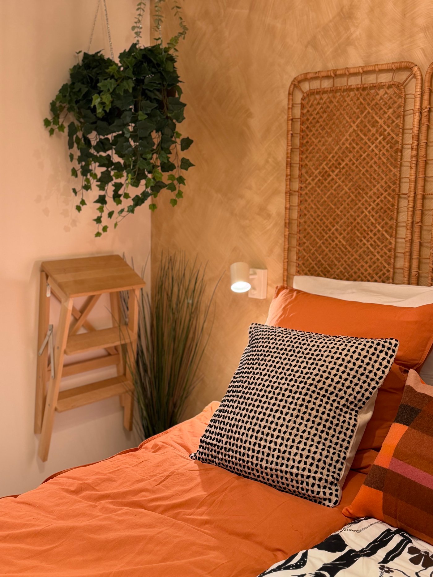 une chambre à coucher harmonieuse, dans les tonalités de terracotta et bois, un marchepied accroché au mur et une plante artificielle suspendue