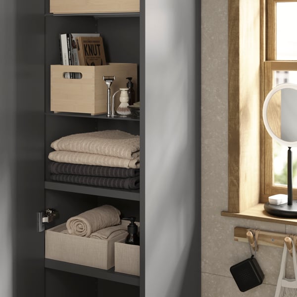 An open HAVBÄCK wall cabinet in dark grey with three shelves. Folded towels and boxes filled with men’s grooming essentials.