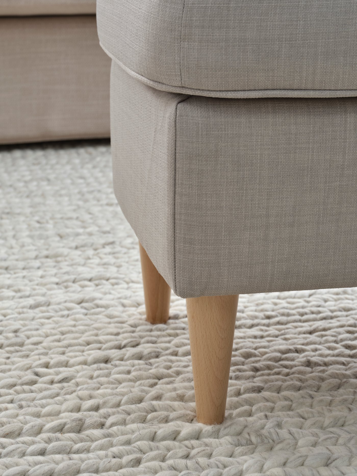 Podnóżek strandmon z drewnianymi nogami stojący na beżowym dywanie.