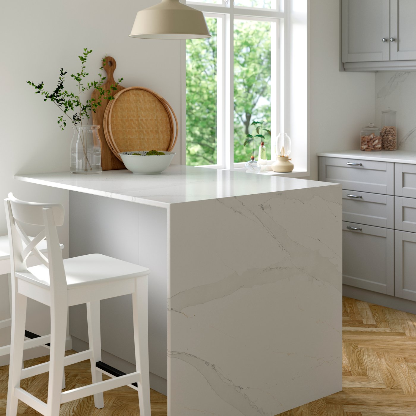 Bright white kitchen with marble island, stool, cutting boards and sunlit window with greenery.