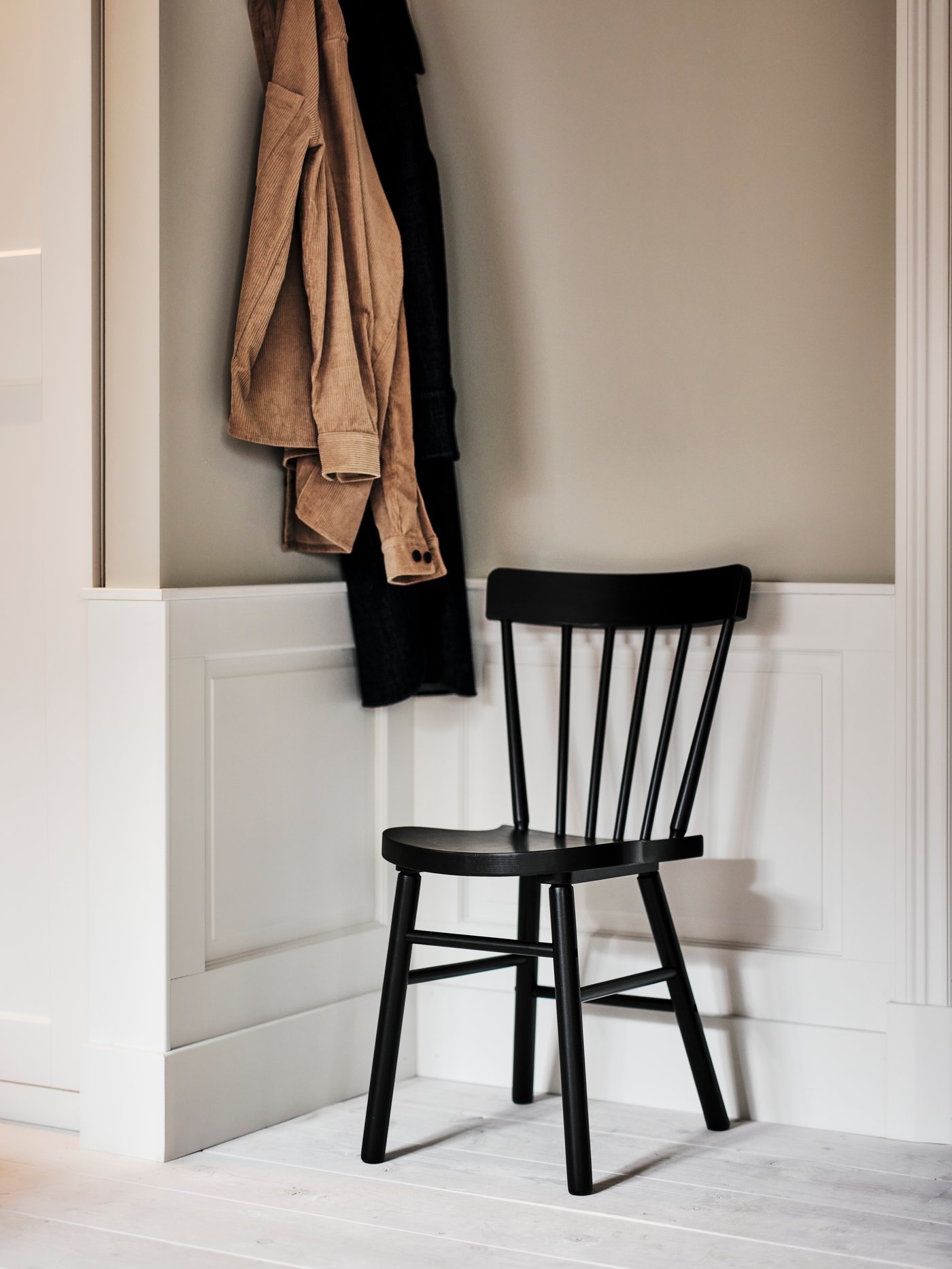 A corner of a room with beige and black items of clothing hanging from a wall next to a black NORRARYD chair.