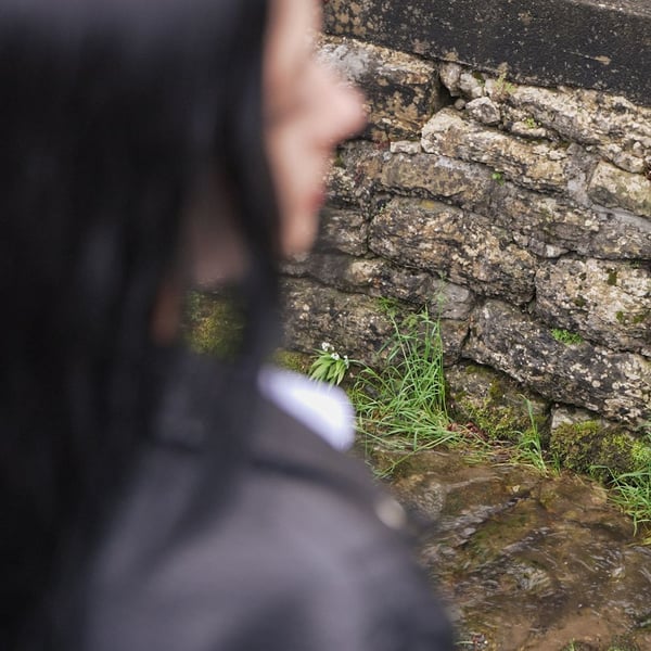 Una ragazza passeggia all’aperto, ma l'obiettivo si concentra sull'acciottolato.