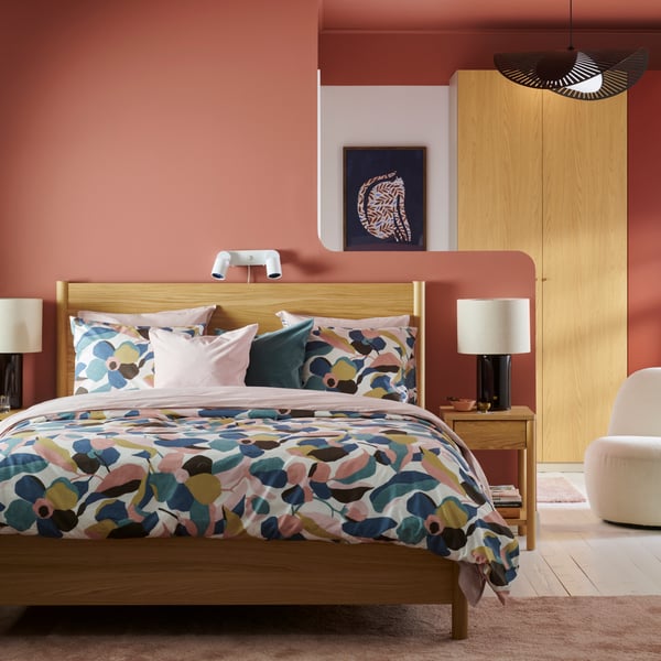A bedroom with orange walls and a light wood TONSTAD bed dressed in bright patterned VIDEOXBÄR bedding.
