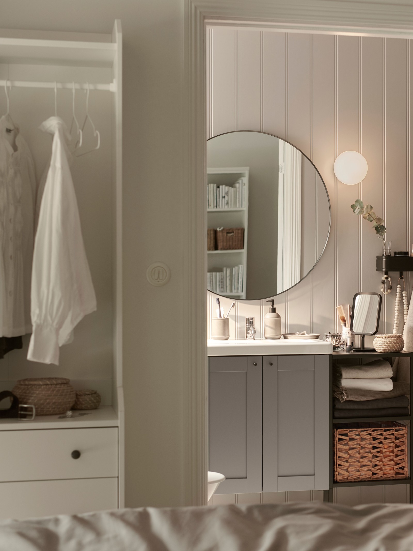 Un vanitorio ENHET/TVÄLLEN con dos puertas con un espejo redondo encima, en un baño pequeño junto a un dormitorio.