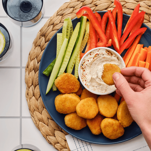 SLAGVERK panerte hvetebaserte biter, ei skål med dipp, agurk og paprika på en blå tallerken.