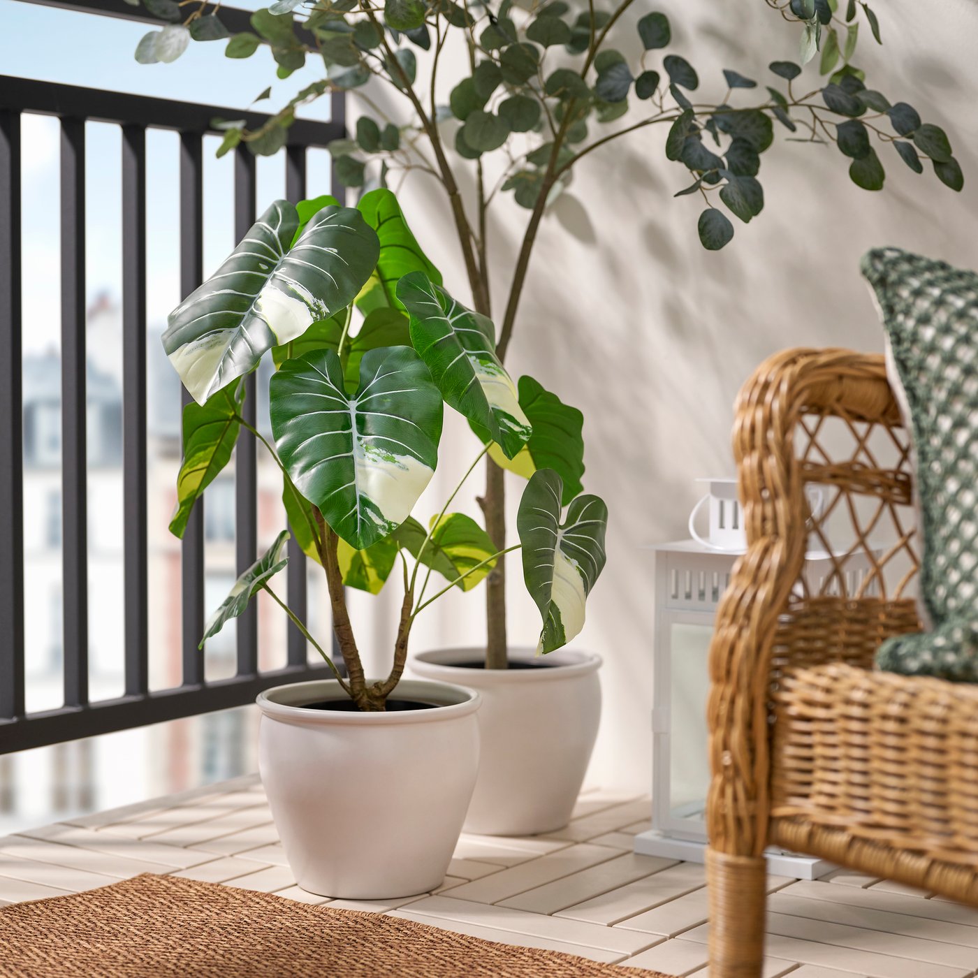 Planta artificial FEJKA tipo alocasia para interior y exterior, colocada en una terraza junto a otras plantas en maceta y muebles de exterior.