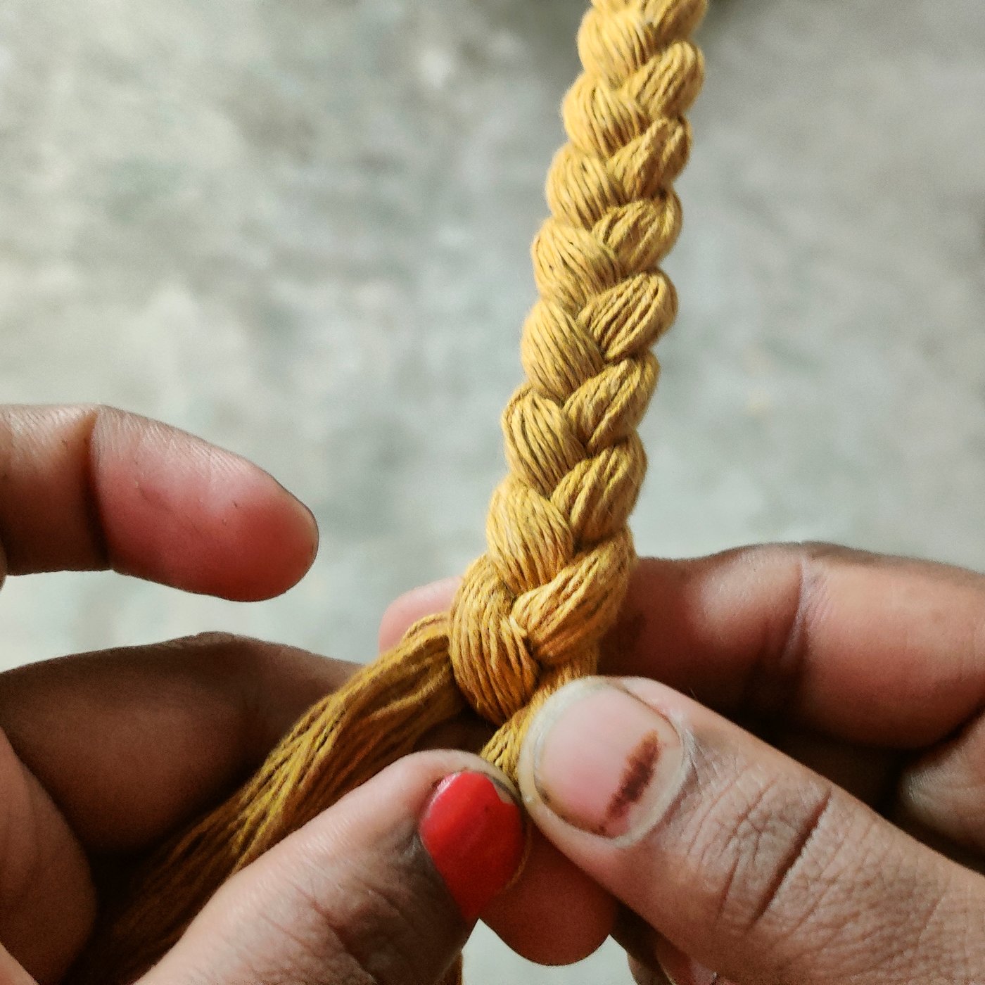 A close-up of two hands braiding some yellow strings against a light grey background.