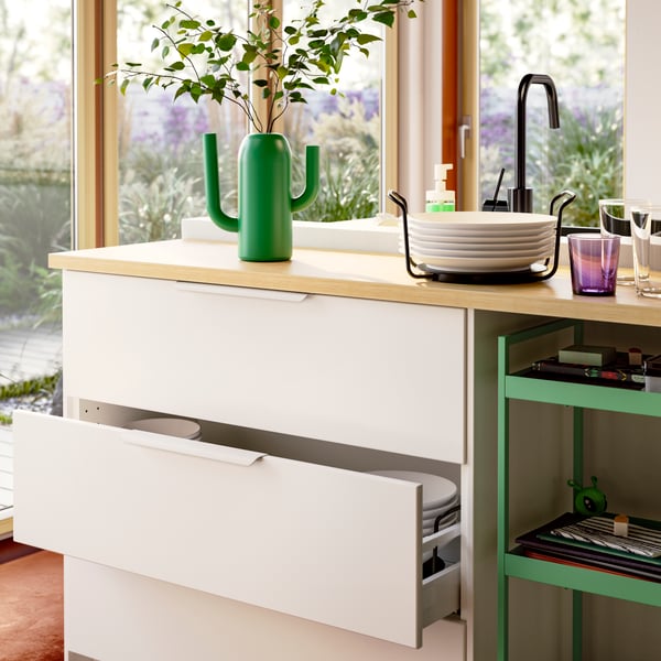Kitchen storage with VEDDINGE white drawer fronts, one is open, and an UPPDATERA plate holder containing plates.