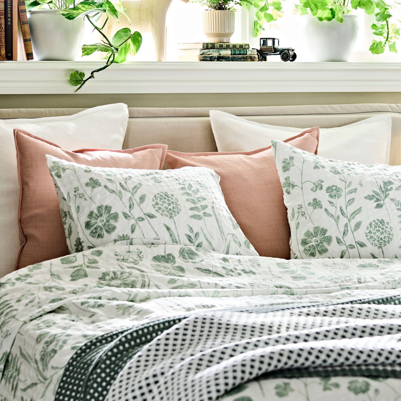 En säng, prydligt bäddad med NÅLBJÖRNBÄR påslakan och örngott samt prydnadskuddar i vitt.