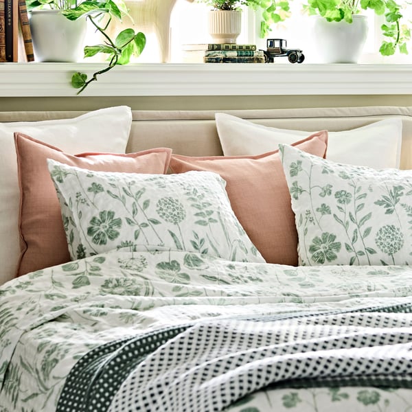 En säng, prydligt bäddad med NÅLBJÖRNBÄR påslakan och örngott samt dekorationskuddar i vitt.