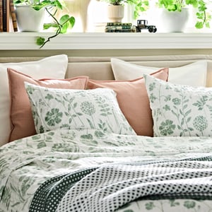 Ei seng, pent redd opp med NÅLBJÖRNBÄR dynetrekk og putevar og dekorative puter i hvitt.