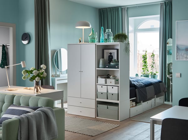 Einzimmerappartment in hellen Grüntönen, einem Sofa in Hellgrün und einem weißen Bettgestell mit Aufbewahrung