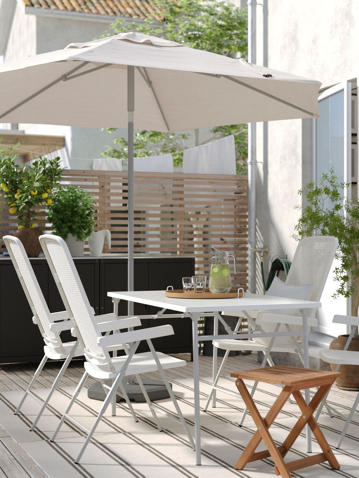 Taras z białymi meblami ogrodowymi TORPARÖ i dużym parasolem.