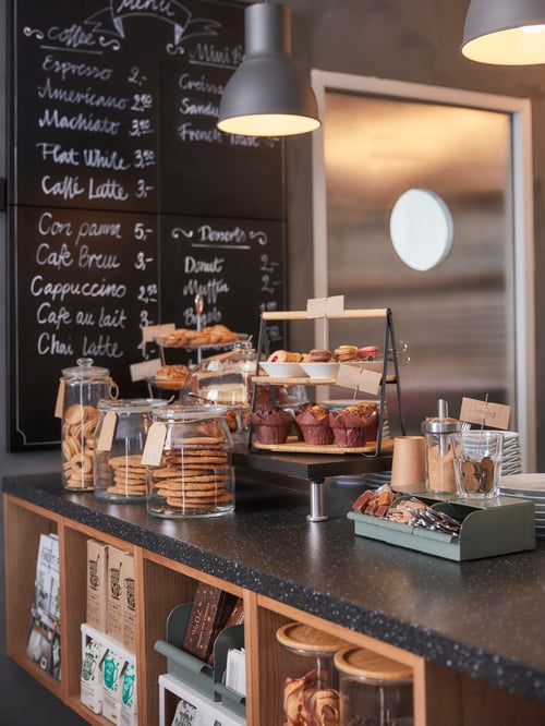 Multiple, beige wine shelves under a black worktop with a box, serving trays and jars with lid on the surface. 