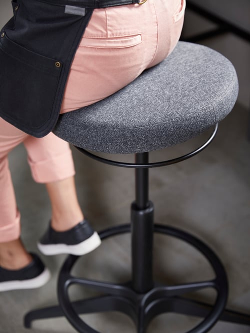 Imagini de aproape cu o femeie cu pantaloni roz, sprijinită pe un suport gri, activ, cu un picior pe suportul pentru picioare.