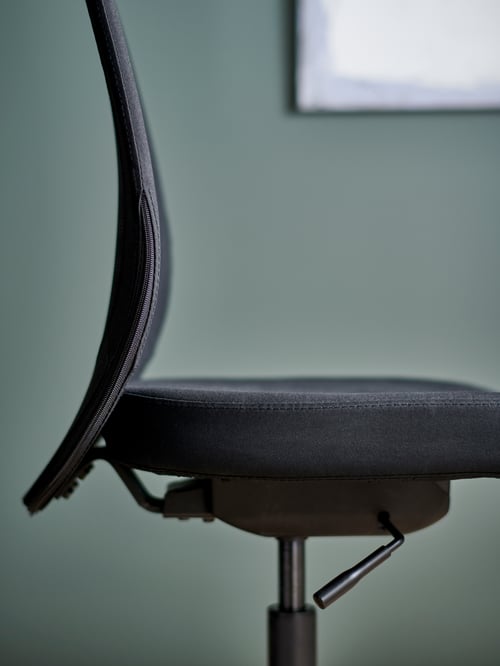 Un prim-plan al unui scaun de birou negru din poliester și oțel, cu mecanism de tensionare și înălțime reglabilă.