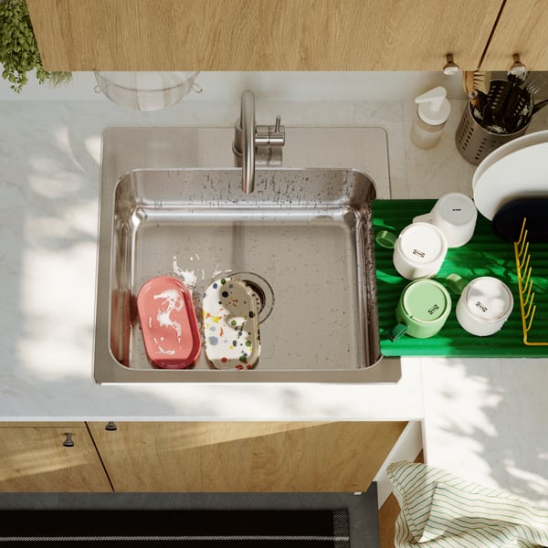 A stainless steel LÅNGUDDEN inset sink with a single bowl, containing two washing-up sponges, surrounded by kitchen items.