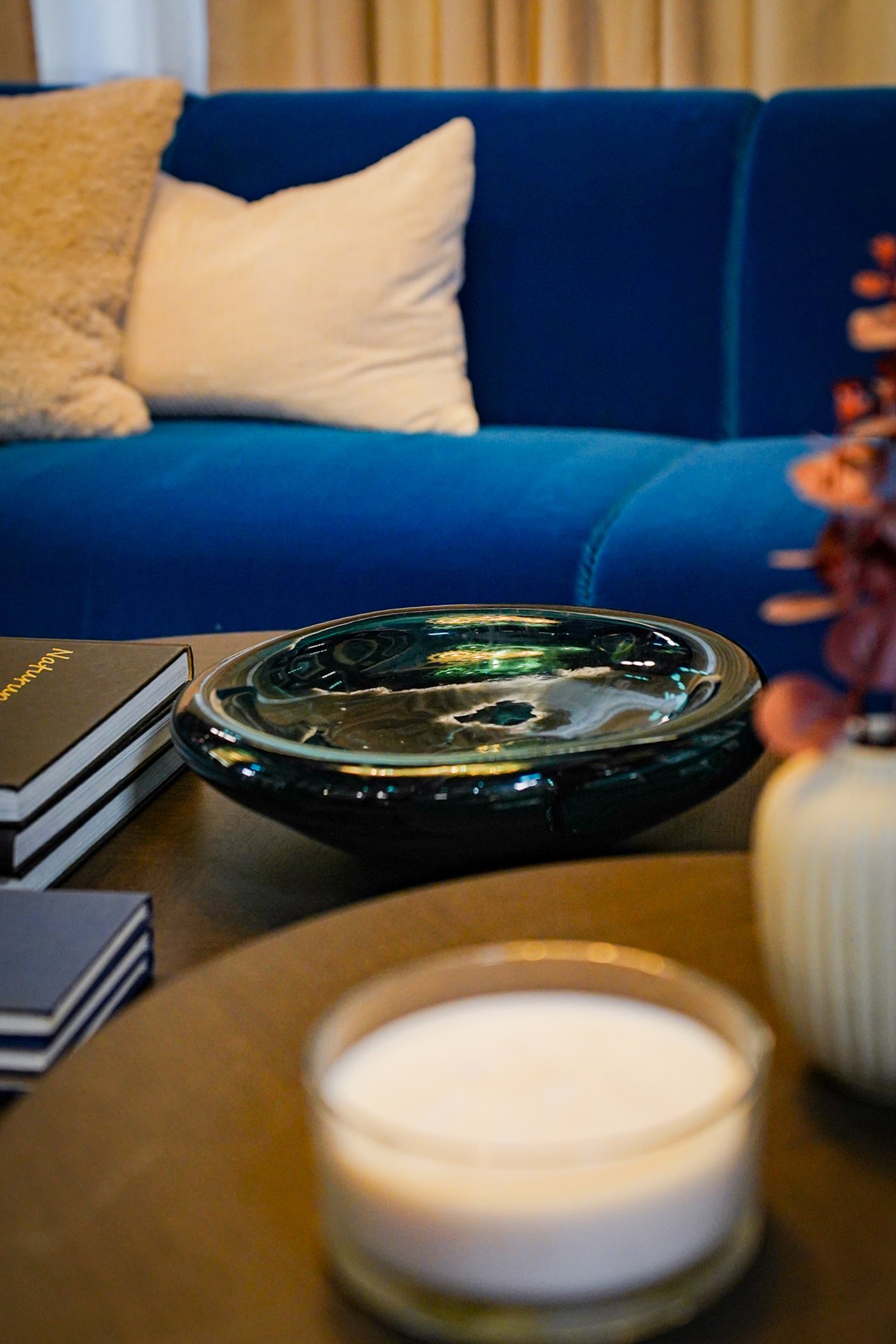 Curious Library room setting at IKEA Tampines, featuring close-up of a dark blue-turquoise STOCKHOLM 2025 bowl and LOTSFÅGEL scented candle in glass on top of a STOCKHOLM 2025 coffee table.