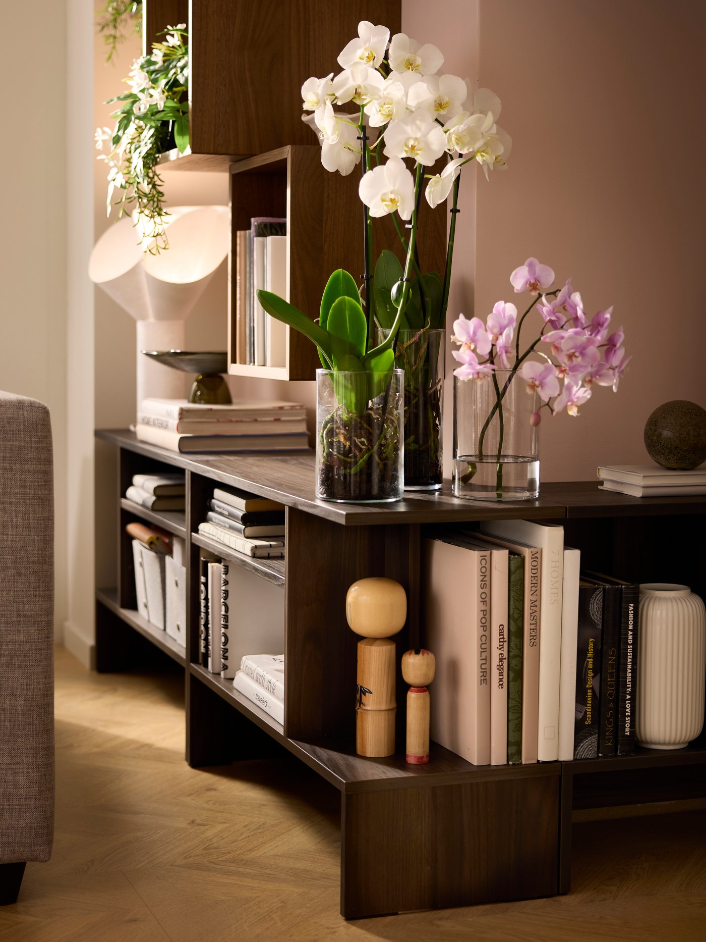 HOLMERUD Beistelltische, gefüllt mit Büchern, Dekoartikeln und Pflanzen, folgen den Konturen einer Außenecke in einem sonnendurchfluteten Raum.