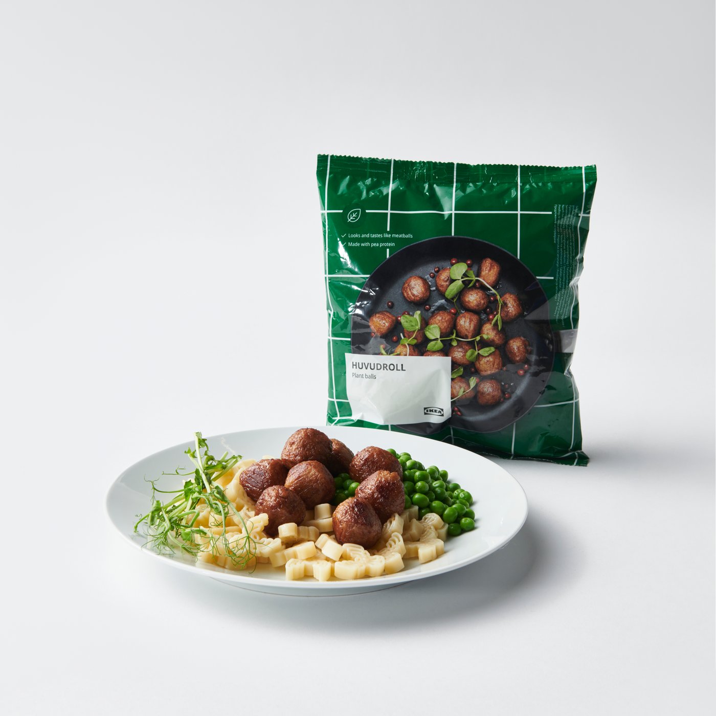 Close up of a white plate with HUVUDROLL plant balls served with pasta and peas. HUVUDROLL package in the background.