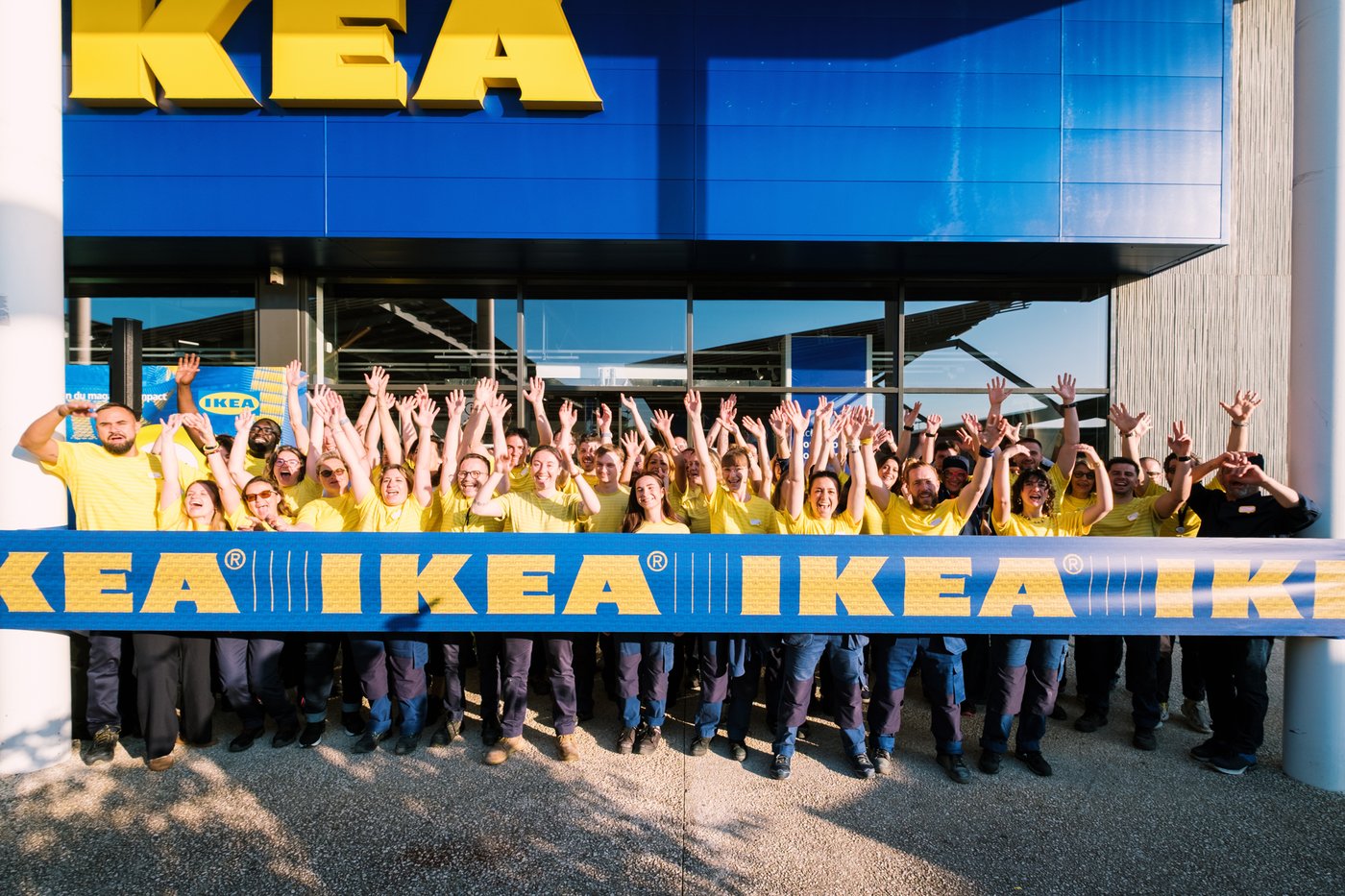Inauguration du magasin IKEA Limoges avec en arrière plan le magasin et devant de très nombreux collaborateurs en tenue IKEA jaune, levant les bras devant un bandeau bleu avec inscrit IKEA en jaune