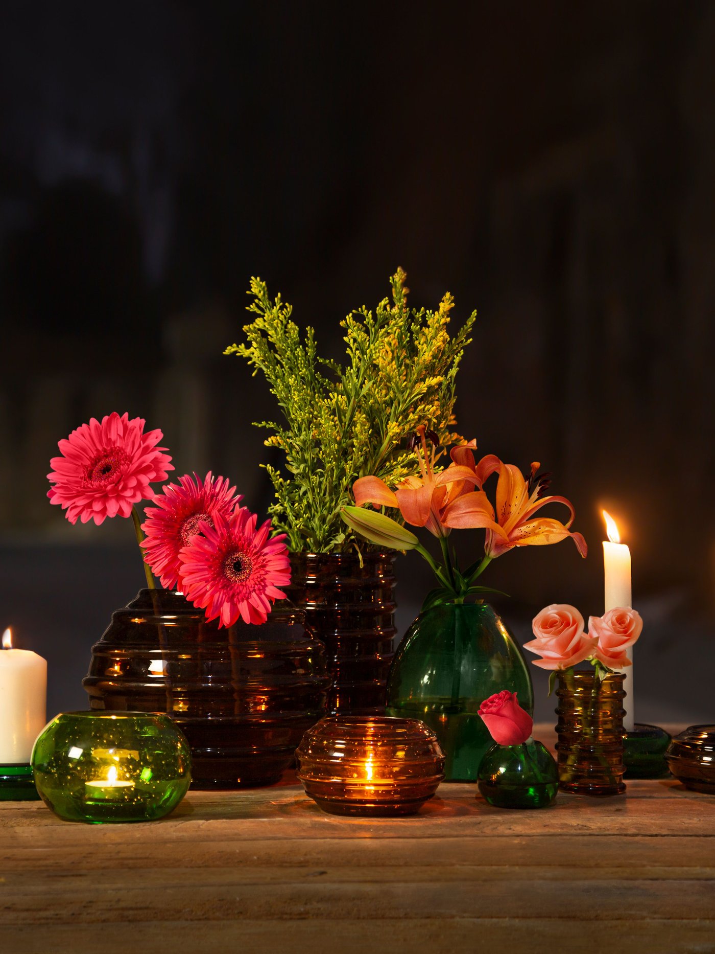 HÄNGBJÖRK Vasen und Kerzenständer stehen in einem dunklen Raum auf einer Tischplatte.
