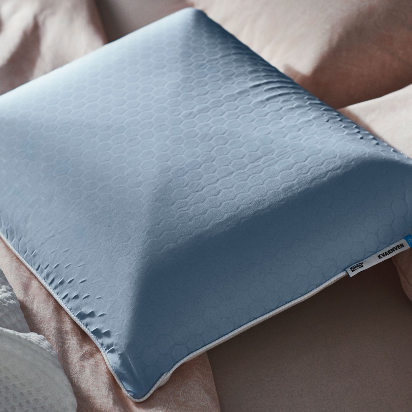 En ergonomisk KVARNVEN kudde utan örngott ligger ovanpå ett lätt skrynkligt täcke.