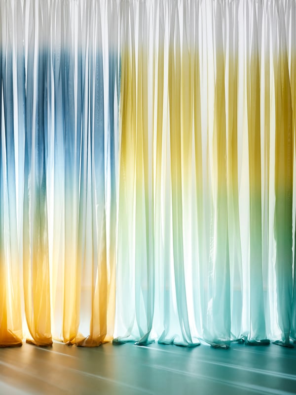 Floor-to-ceiling GLASÖRT sheer curtains with a rainbow colour fade. There are reflections from the light on the floor.