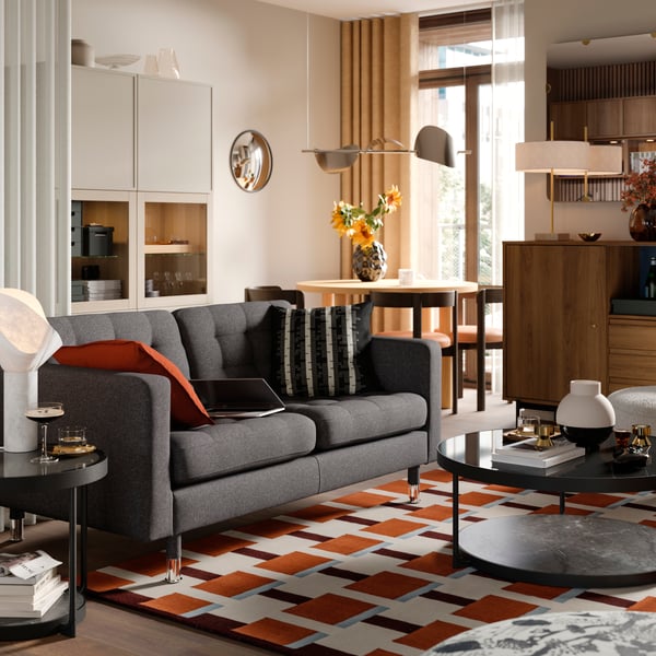 Dwuosobowa sofa z tkaninyustawiona w pokoju dziennym w pobliżu mebli do przechowywania BESTÅ i szafki RÅDMANSJÖ.