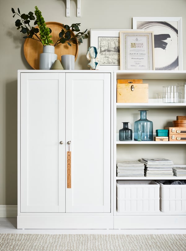 IKEA HAVSTA white cabinet, with plinth, beside open storage, with plants, pots, pictures, baskets and decorative accessories.