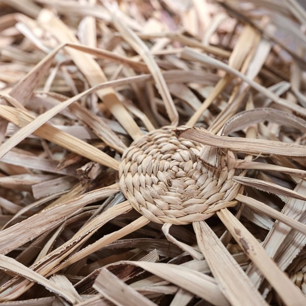 A half-finished sample of the MÄVINN wall decoration lies on a pile of dried banana bark fibers.