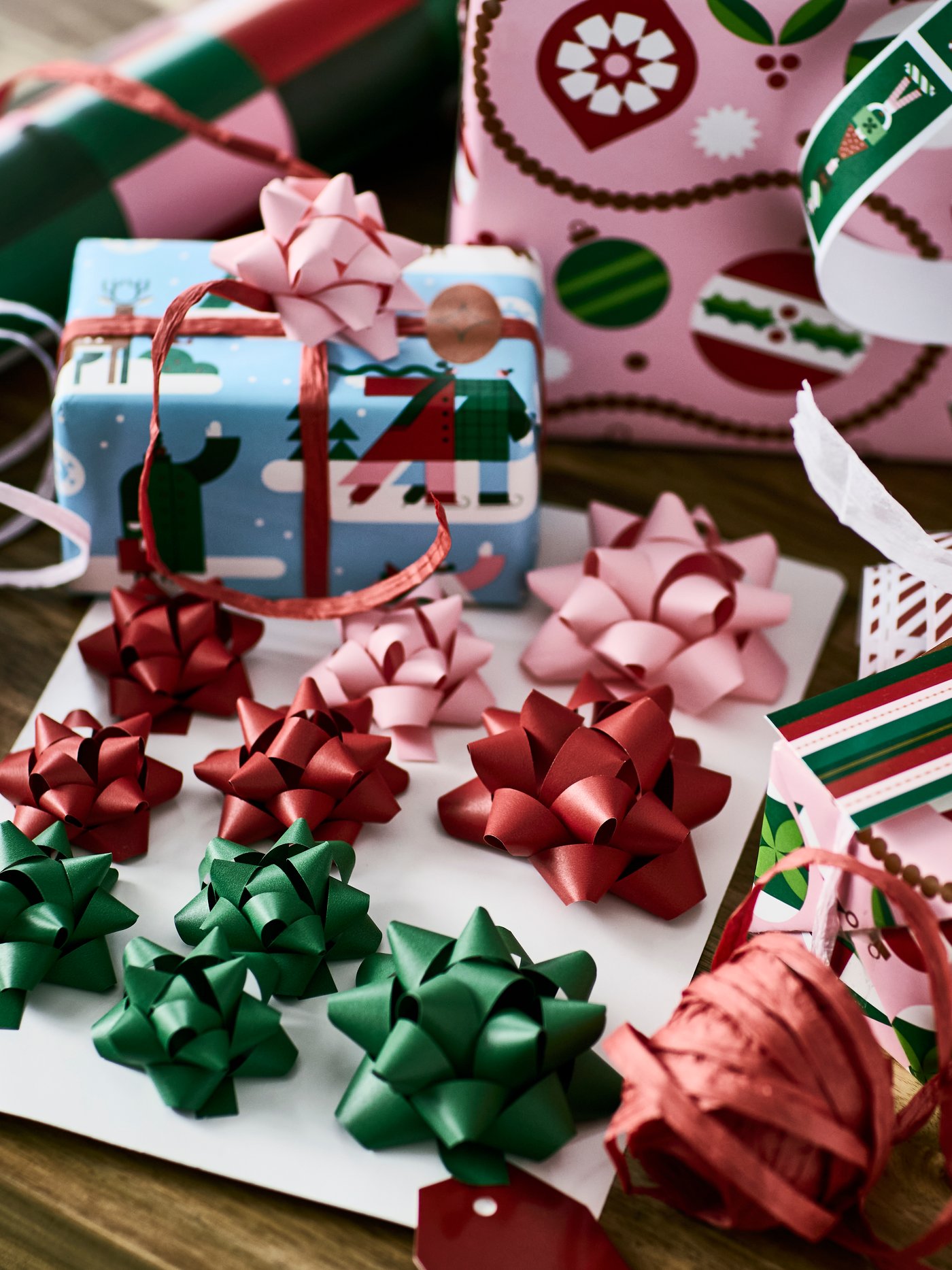 A set of VINTERFINT gift bows in green, red and pink is surrounded by ribbons and wrapped presents and gift wrappers.