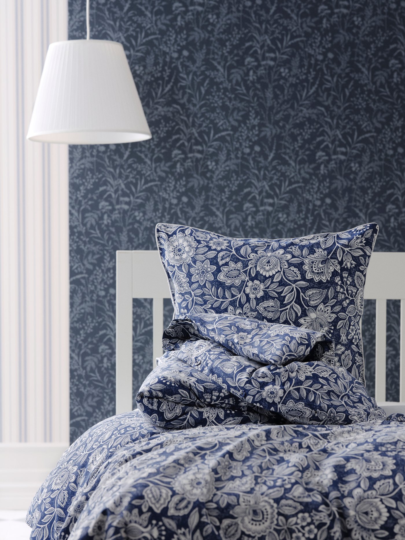 Ropa de cama floral blanca y azul con una pantalla de lámpara blanca sobre la cama.