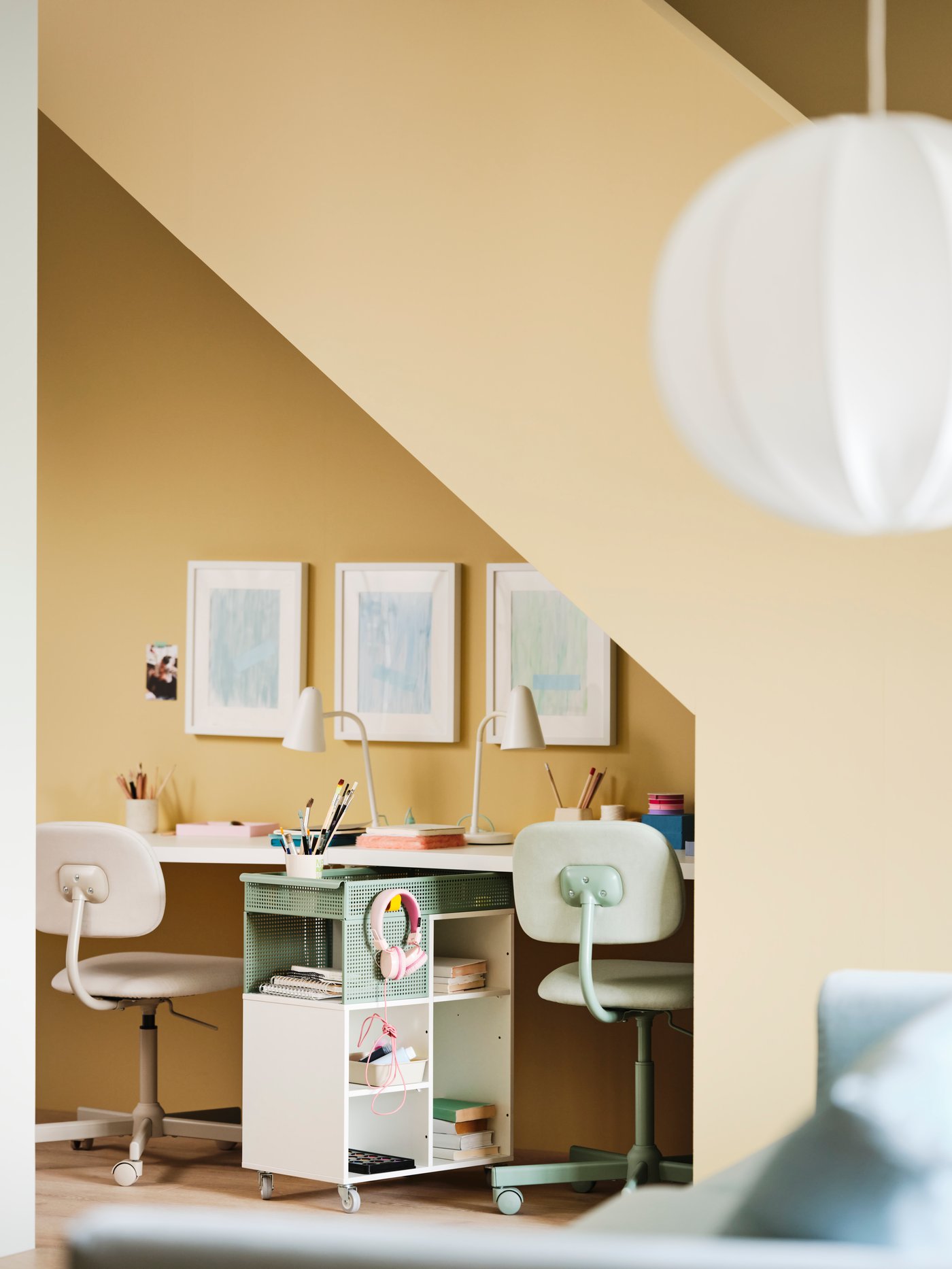 Two BLECKBERGET swivel chairs, desks, desk lamps and an ÖVNING trolley form a study nook under the stairs.