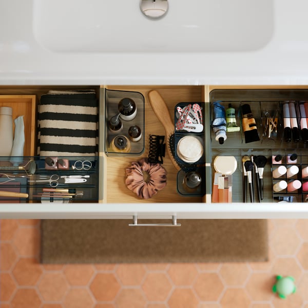 A close-up of a grey VISSLAÅN box with compartments, neatly organised with various beauty products in a bathroom drawer.