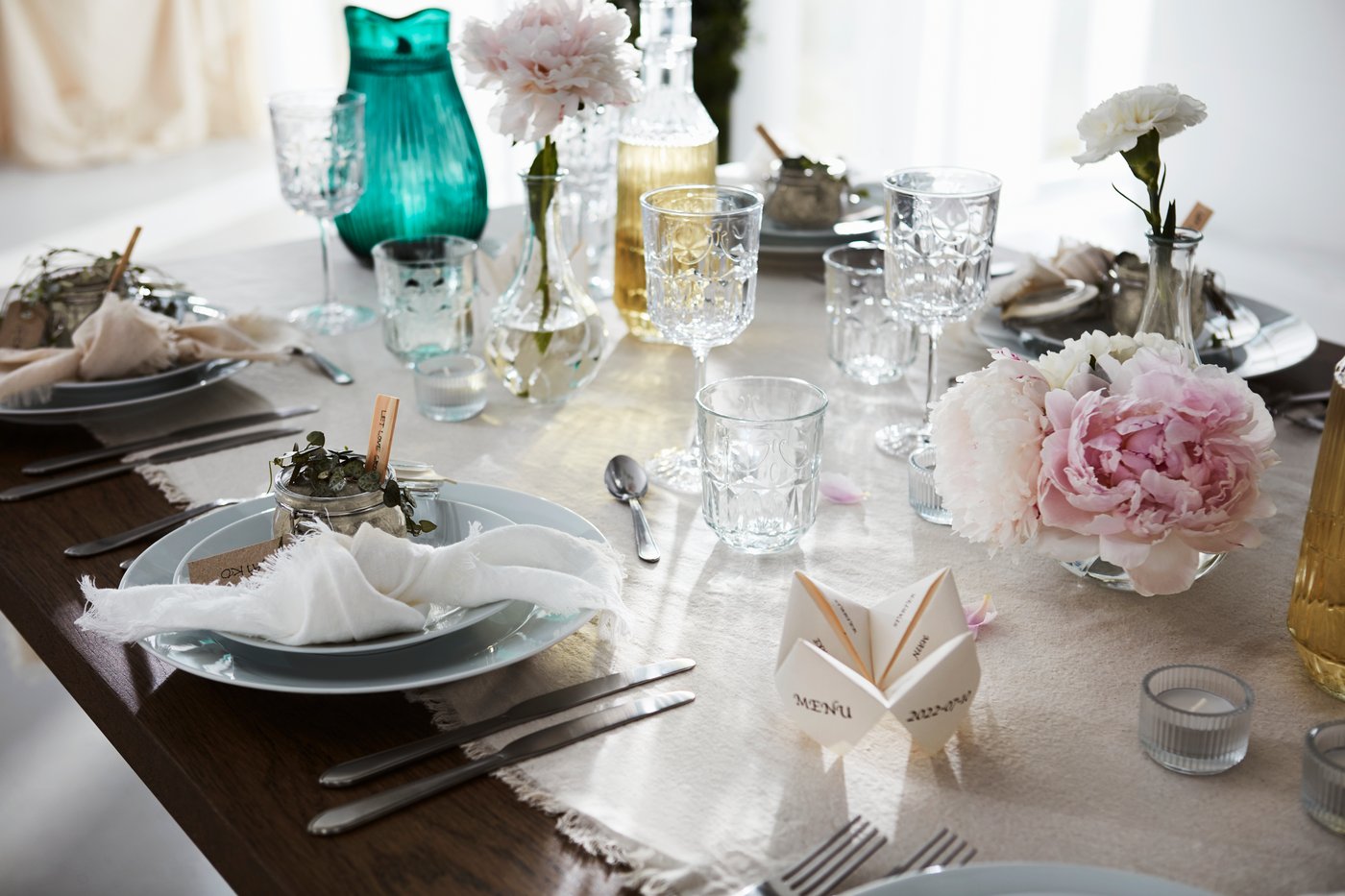 Ett findukat bord dukat för en formell tillställning med en ljus duk, fina glas, tallrikar, bestick och blomsterdekorationer.