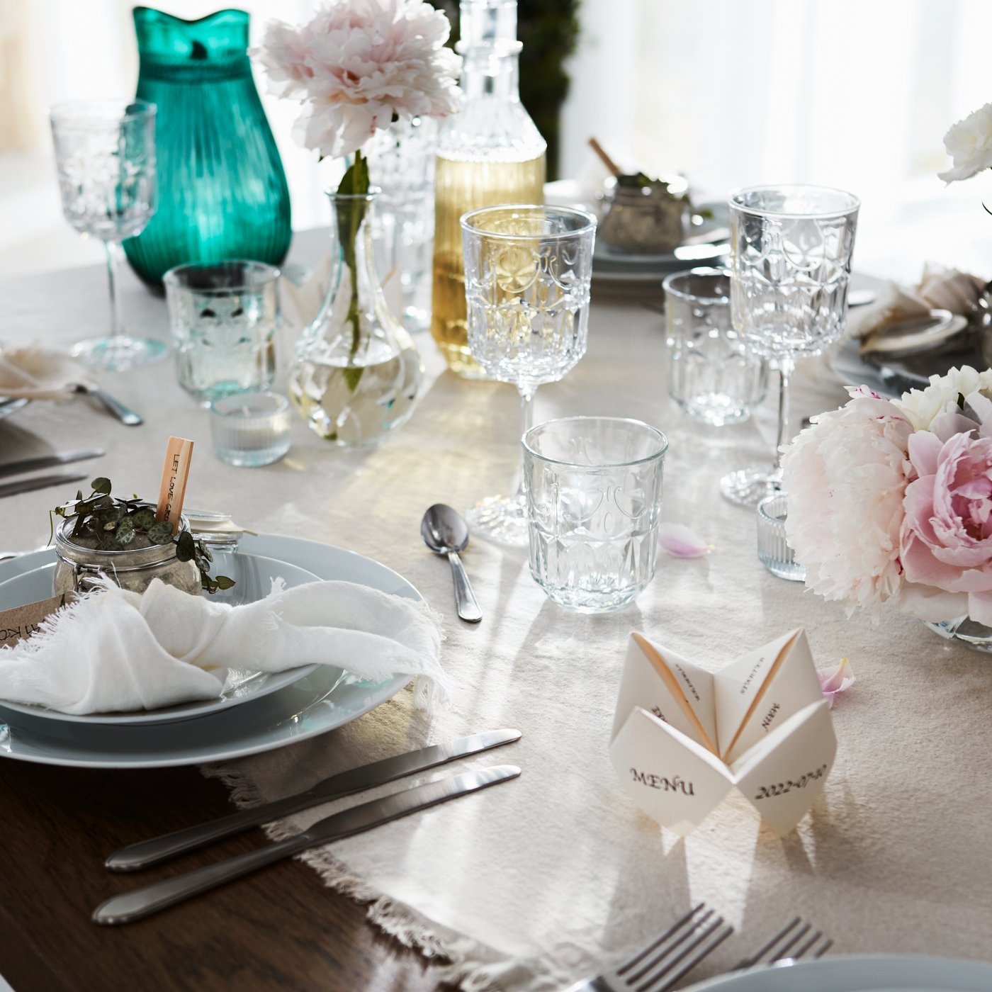 Ett findukat bord dukat för en formell tillställning med en ljus duk, fina glas, tallrikar, bestick och blomsterdekorationer.