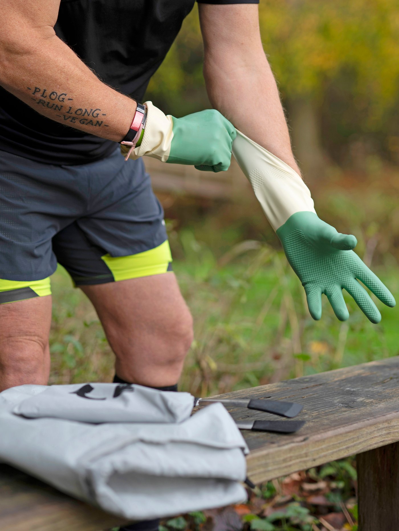 Moški na prostem, oblečen v športna oblačila, si nadeva RINNIG rokavice za čiščenje. Na klopi poleg njega vidimo prazno AJÖSS vrečo za ločevanje odpadkov in IKEA 365+ prijemalko. 